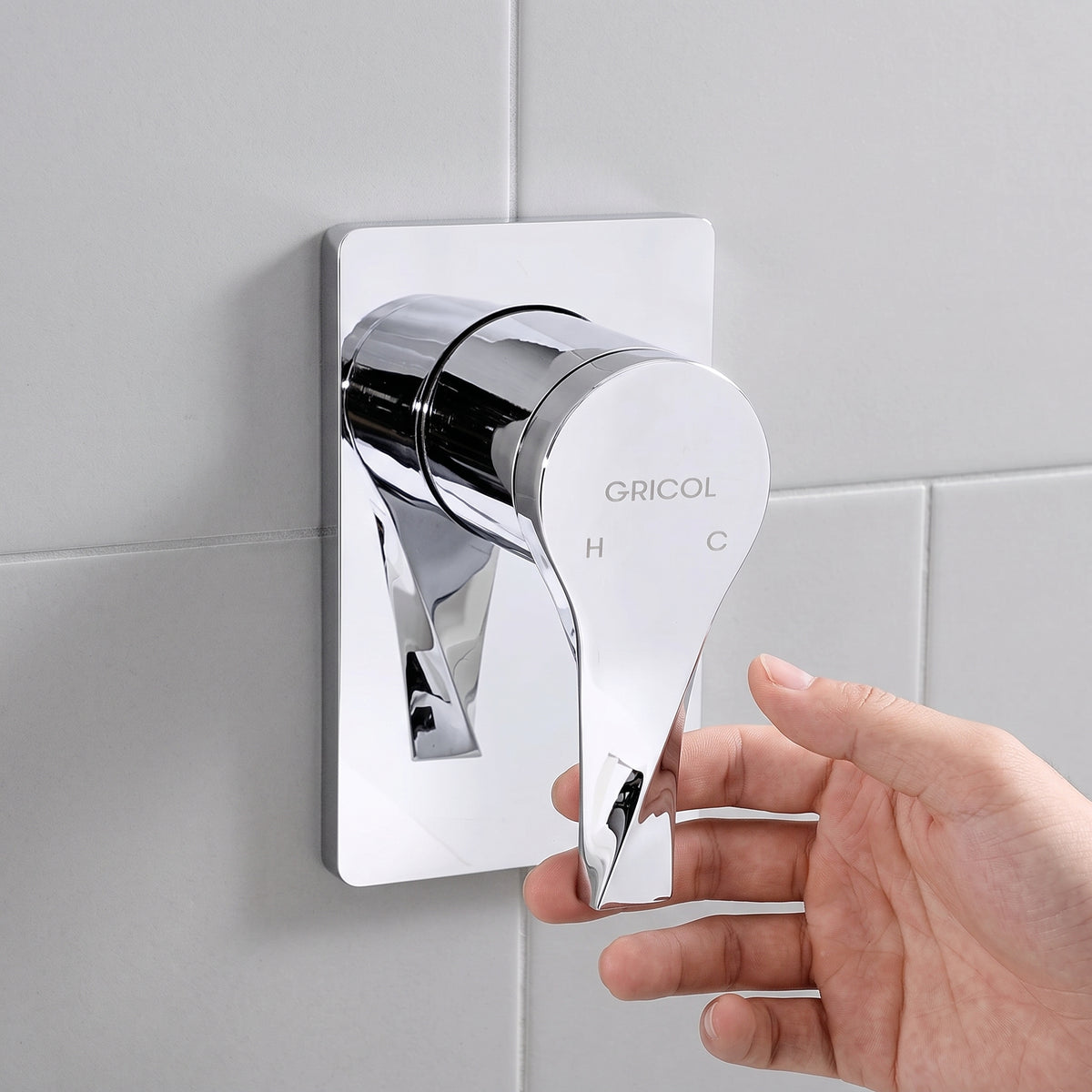 Monomando de ducha Sion con escudo cuadrado acabado cromado, en ambiente de baño claro y la mano de una persona usándolo para su ducha