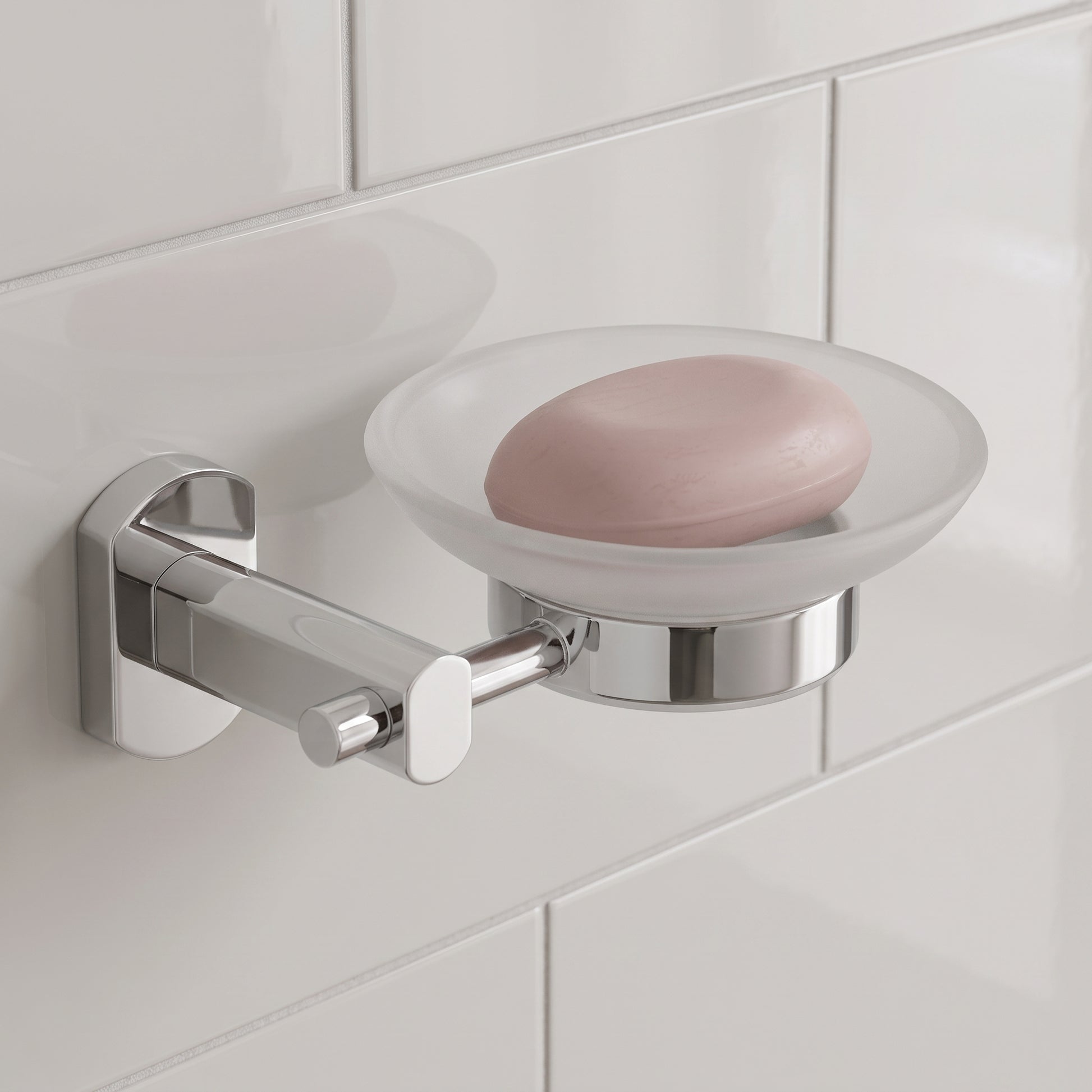 Jabonera de vidrio, metal Portobello en acabado cromado, instalada en un ambiente de baño moderno con un jabón.